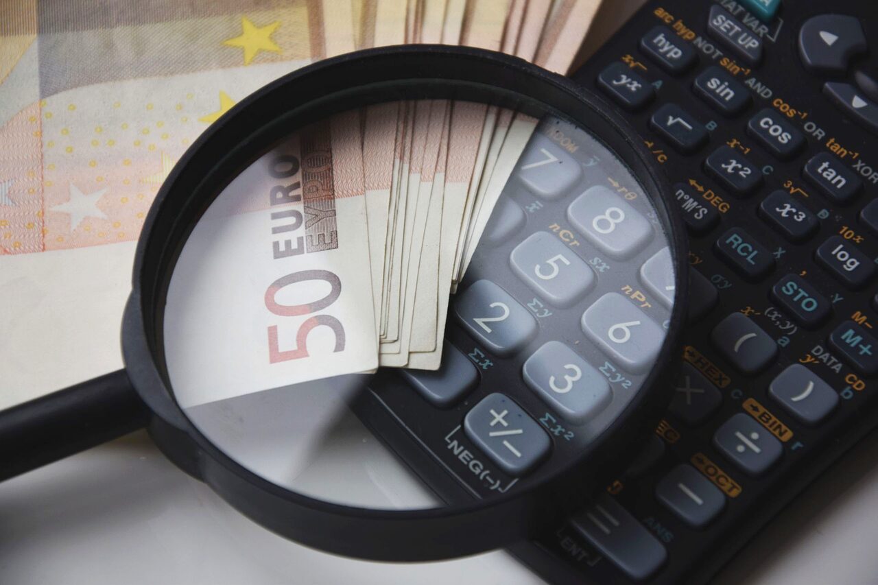 Image featuring magnifying glass on currency and a calculator illustrating the focus on financial assessment in a cost estimation consulting firm