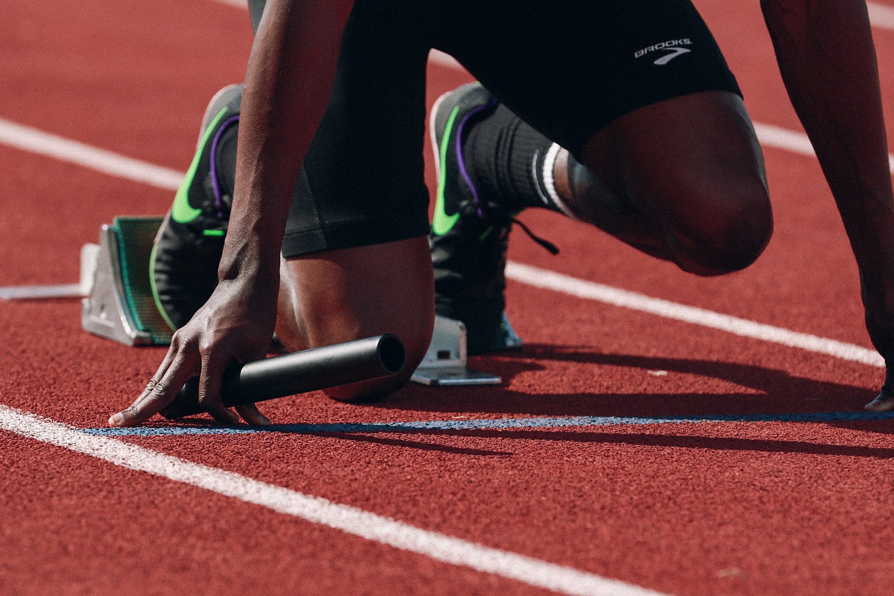 Runner in starting position on a track, holding a relay baton, preparing for a race.