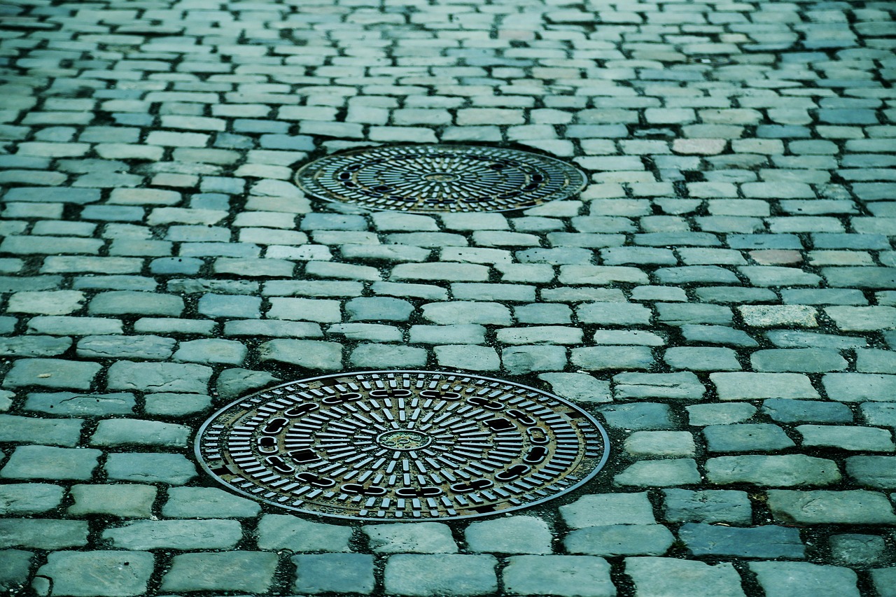 A view of a cobblestone street with two visible manholes, emphasizing the need for regular grounds maintenance services.