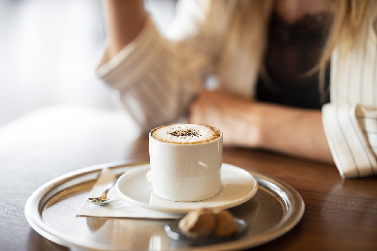 A woman enjoys a cup of coffee while seated at a table, representing a cozy moment in a food and beverage setting.