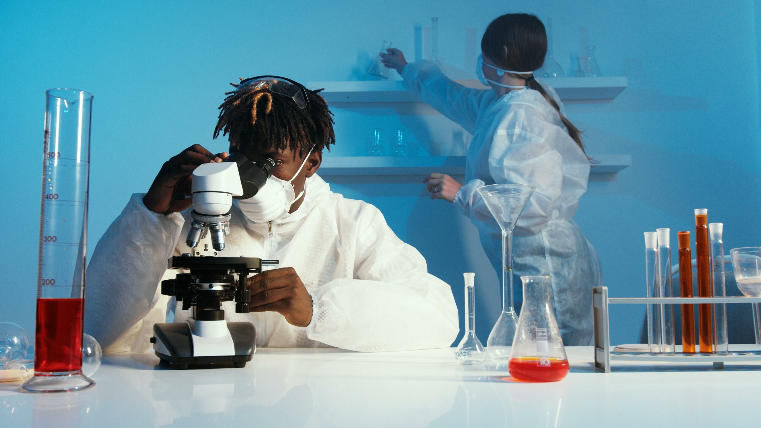 A medical assistant business owner examines a sample through a microscope while wearing a white lab coat in a laboratory setting.