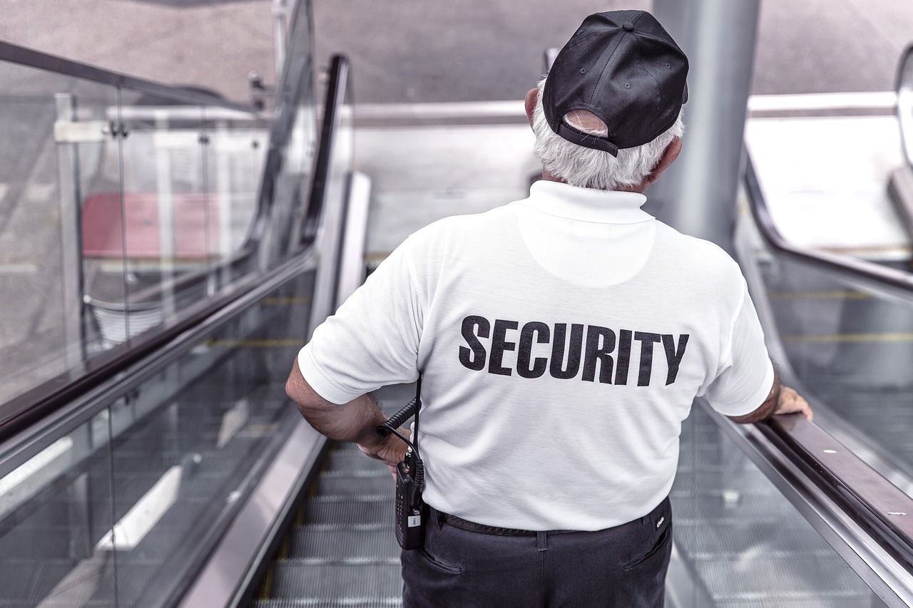 A man in a security shirt stands on an escalator, representing a professional in the security services industry.