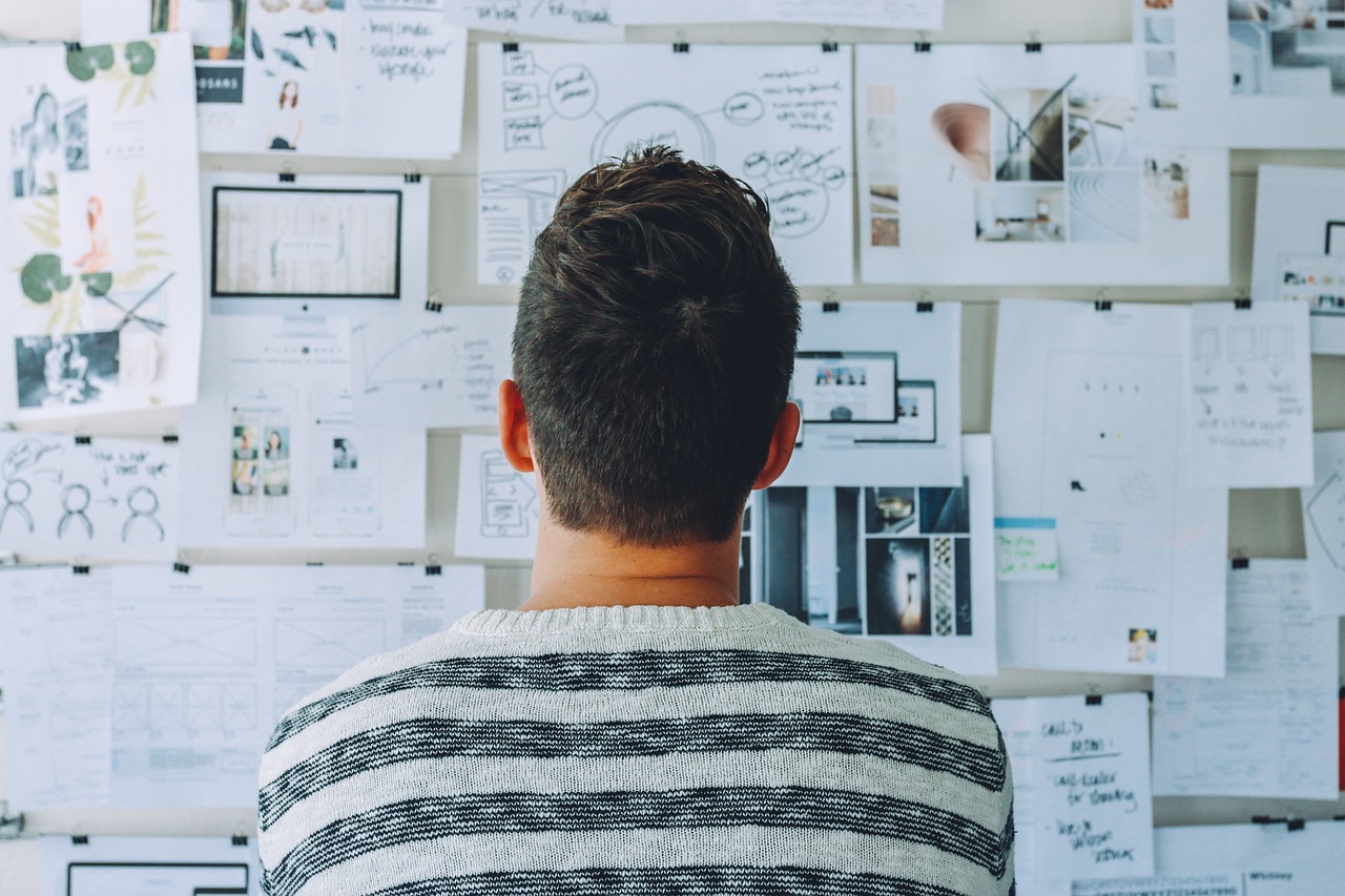 A man observes a wall adorned with various papers, showcasing the creativity of a Set and Exhibit Design Agency.
