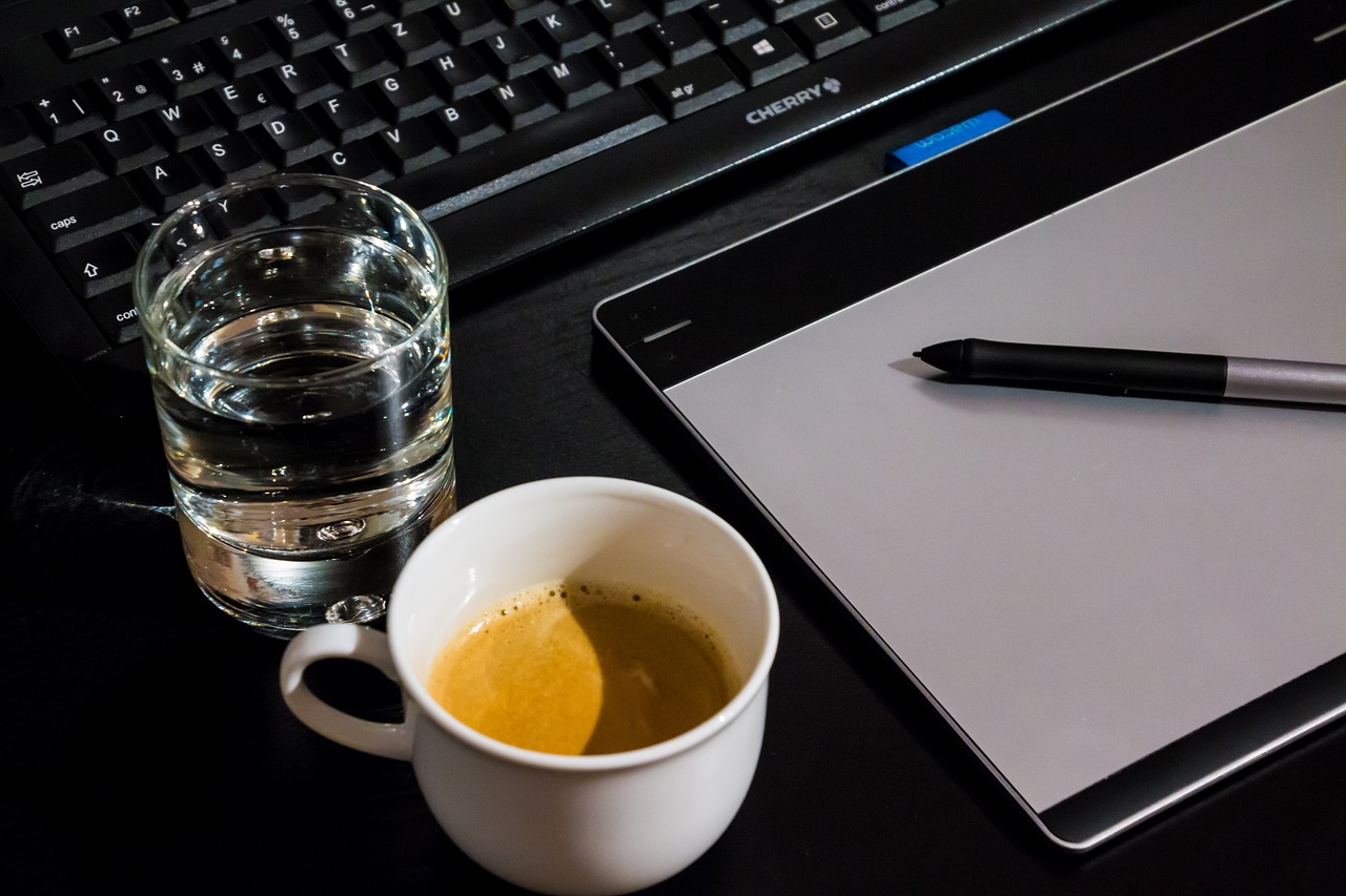 A coffee cup, pen, and laptop arranged on a desk, symbolizing a graphic design studio owner's workspace.