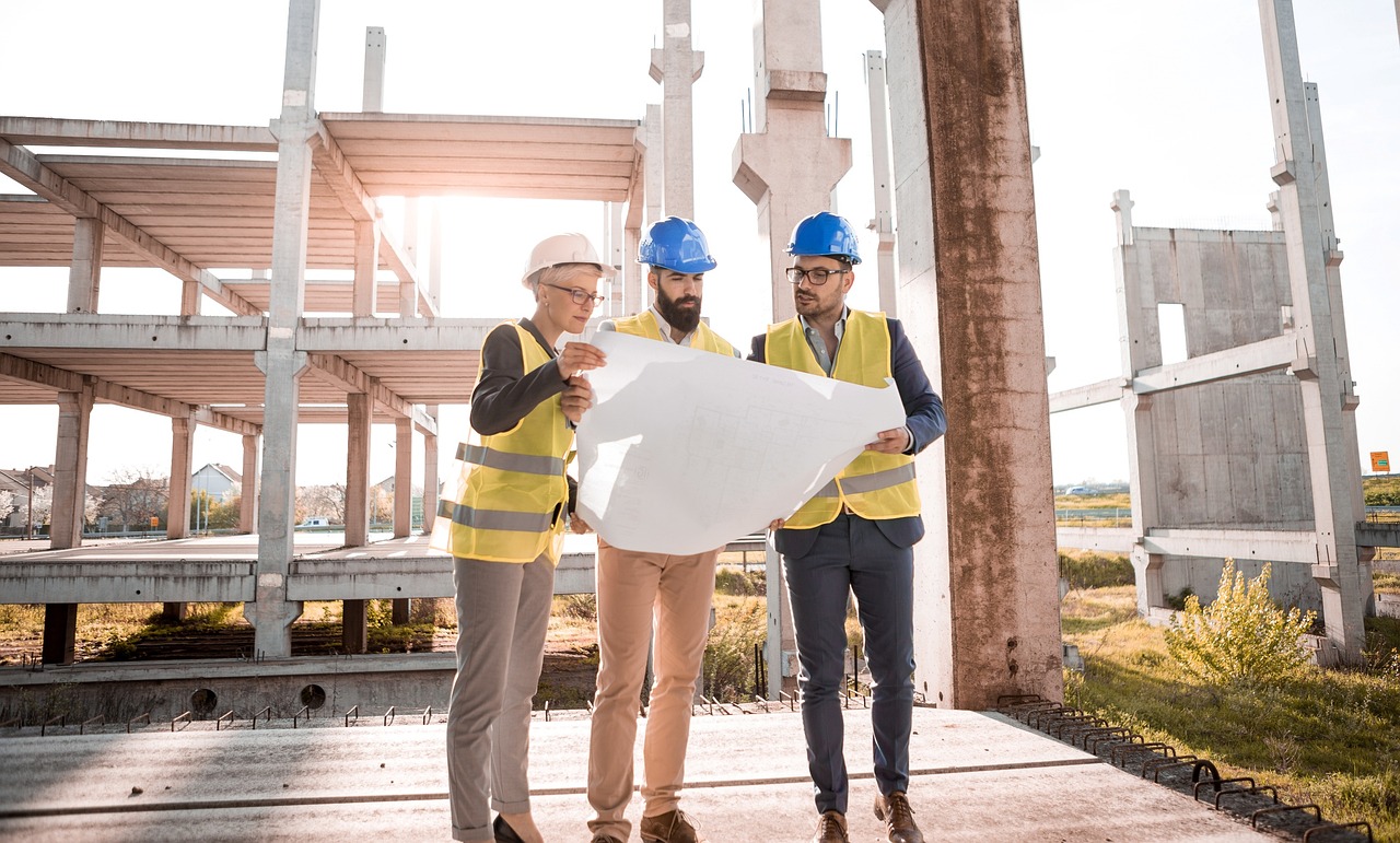 Three construction workers in hard hats and safety vests pose in front of a building, highlighting their professional environment.