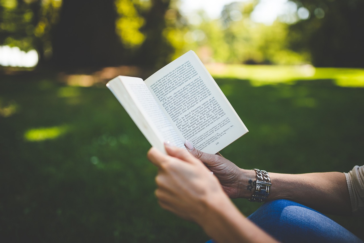 A person engrossed in a book while seated on a bench in a serene park setting, surrounded by greenery.