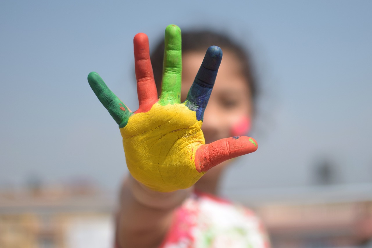 A young child holding up a hand painted in bright, vivid colors—red, yellow, green, and blue—symbolizing creativity, play, and learning in a preschool environment