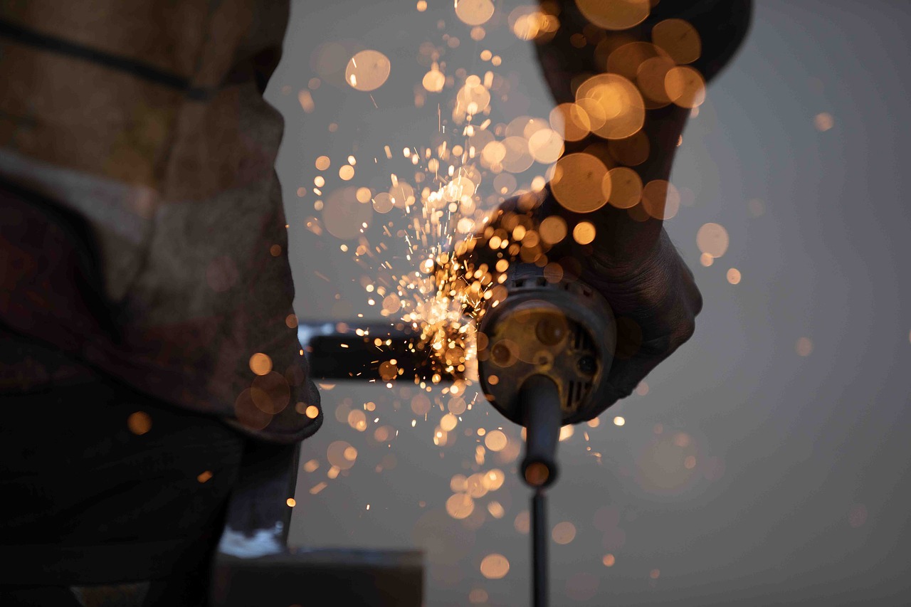 A business owner operates a grinder to cut metal sheets in a fabrication workshop, showcasing skilled craftsmanship.