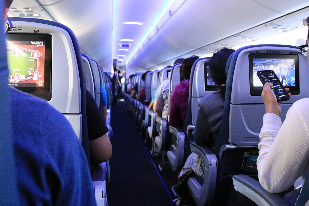 Travelers aboard an airplane, utilizing cell phones, showcasing the intersection of technology and customer care in aviation.