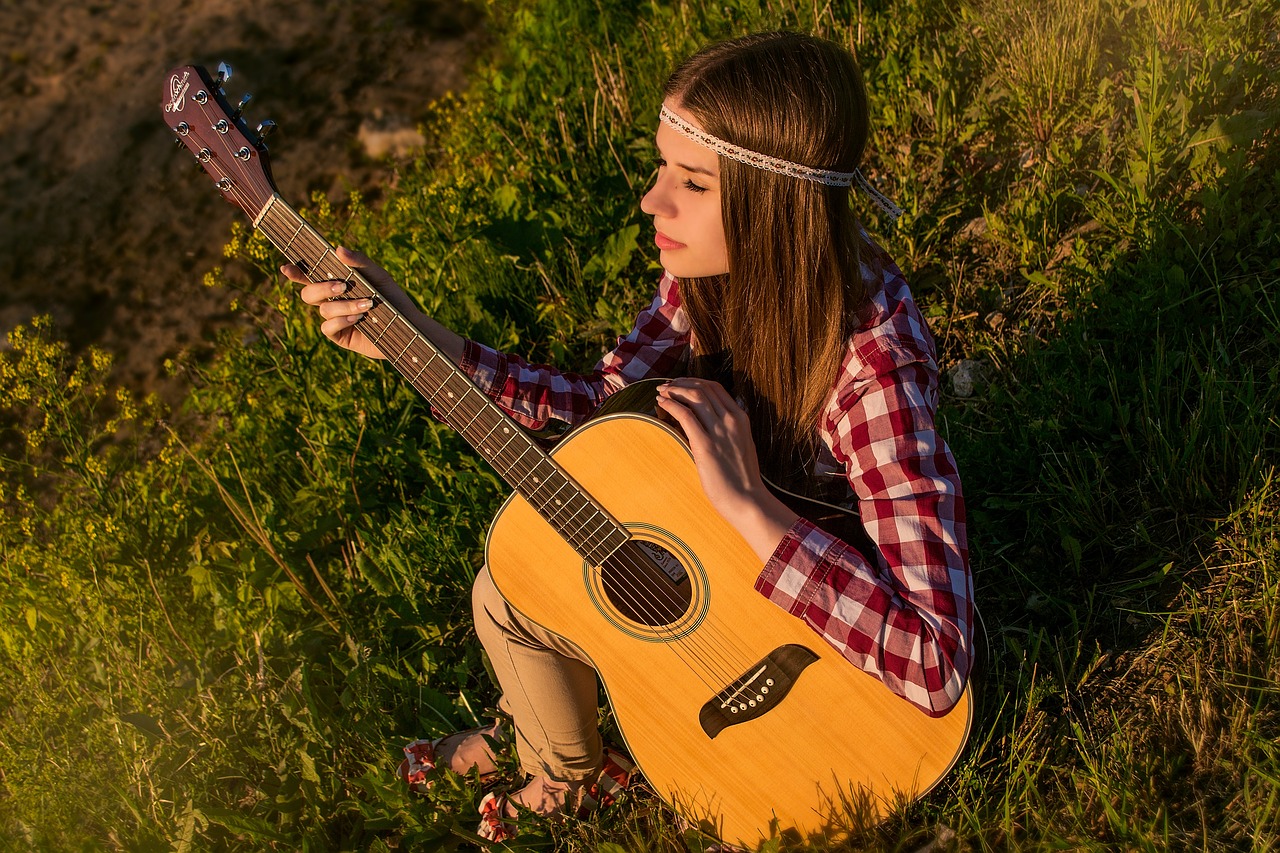 A girl sits on the grass, strumming an acoustic guitar, embodying creativity and passion in her music business journey.