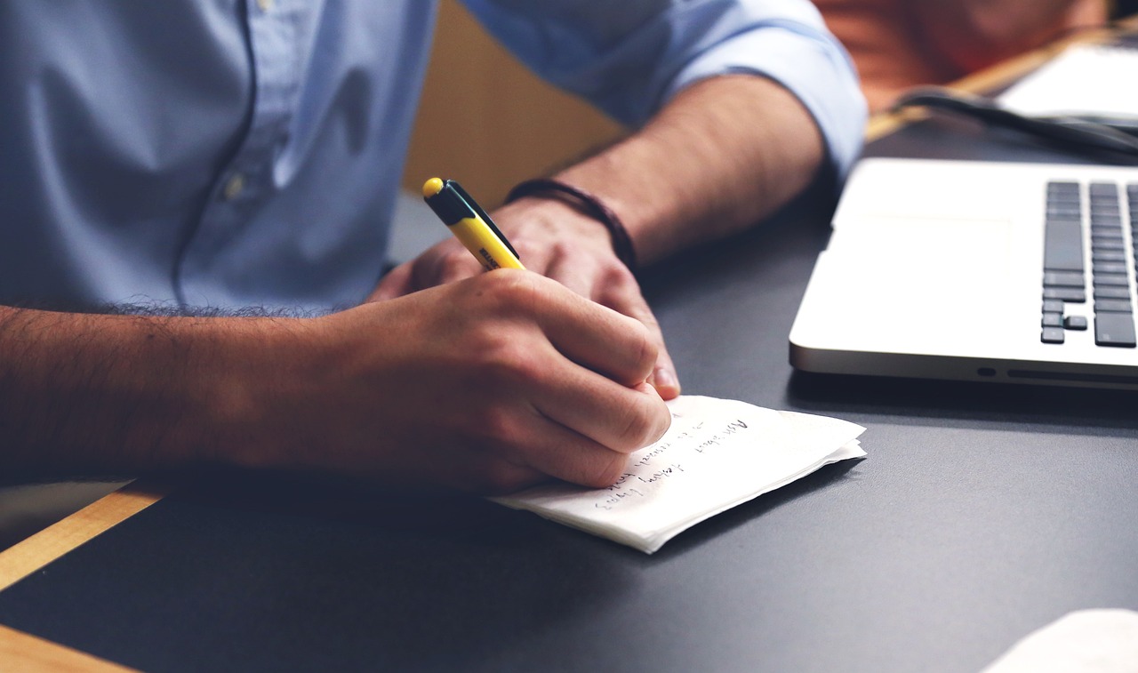 A business owner in technical writing diligently composes notes on paper using a pen, showcasing his expertise and focus.