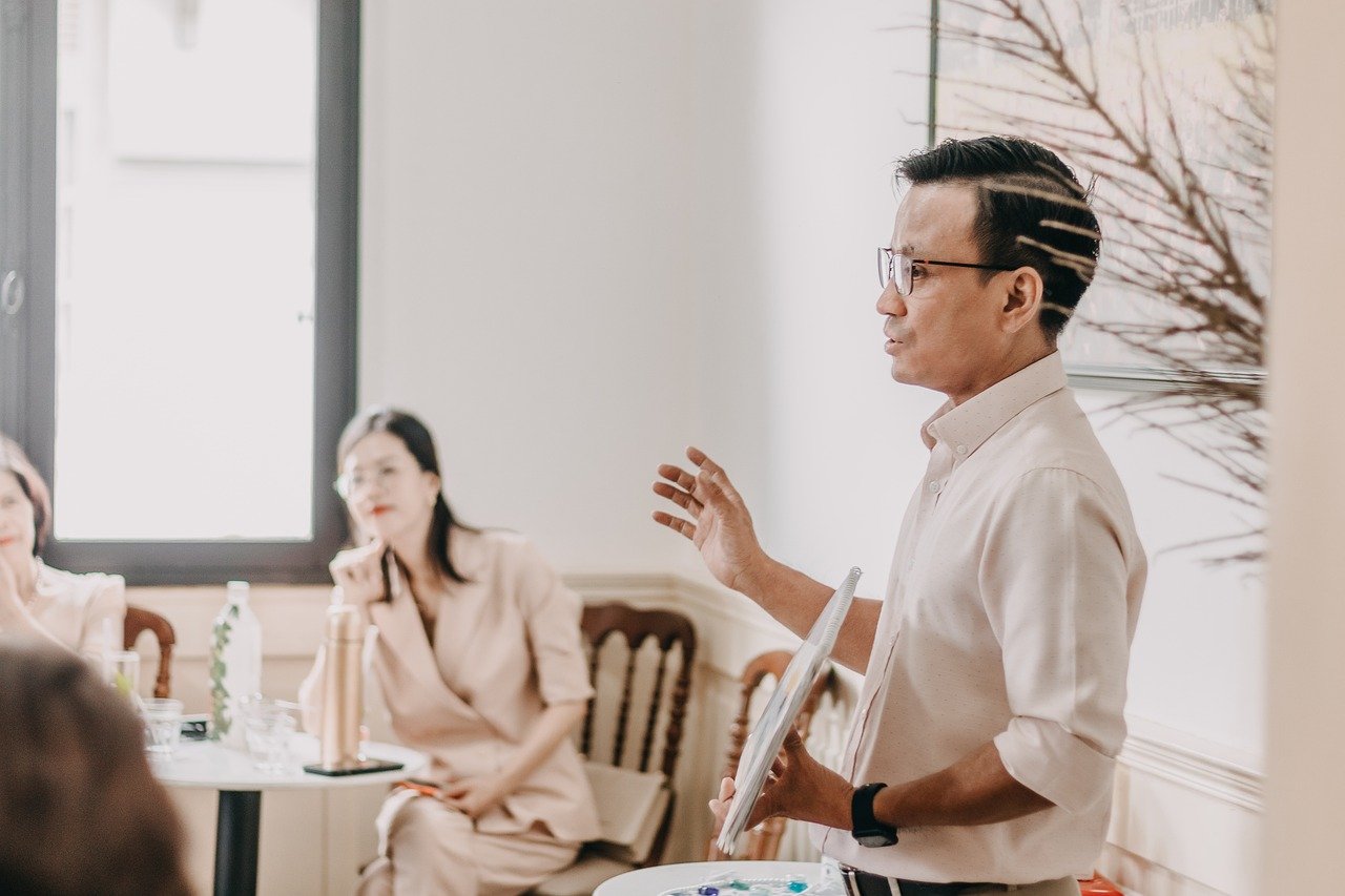 A man presents to an audience, sharing insights on Management Analysis Services in a professional setting.