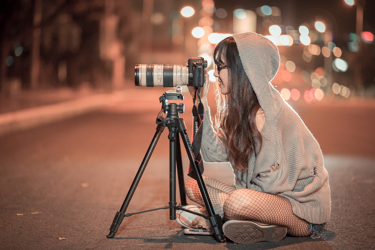 A woman, a photography business owner, sits on the ground with a camera, capturing moments in her creative space.