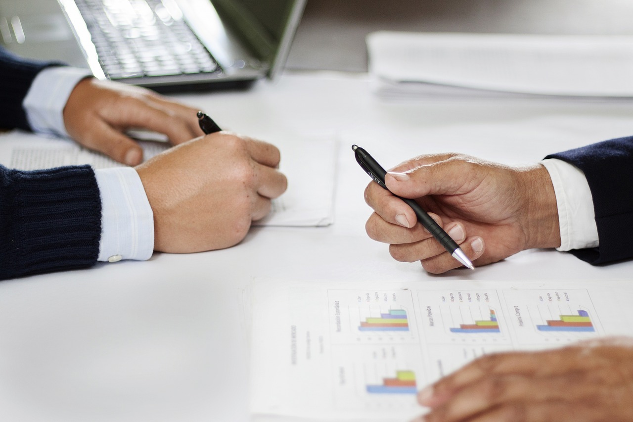 Two business professionals writing on papers with pens, engaged in a discussion about personal financial advisory services.