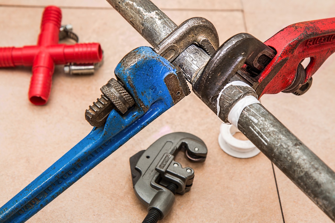 A pair of wrenches and a pipe wrench arranged on a tile floor, symbolizing plumbing and pipefitting services.