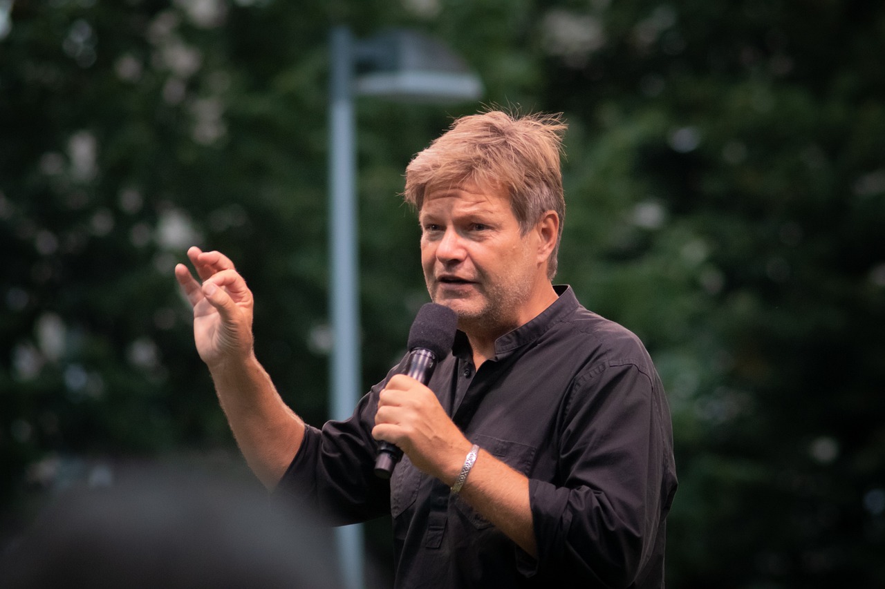 A man, representing an events planning business, delivers a speech into a microphone at an outdoor event, captivating attendees.