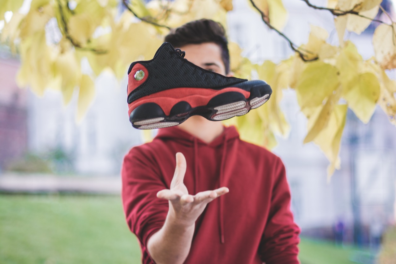 A man, owner of an Advertising Sales Consultancy, proudly displays a pair of sneakers overhead, representing his passion for sales.