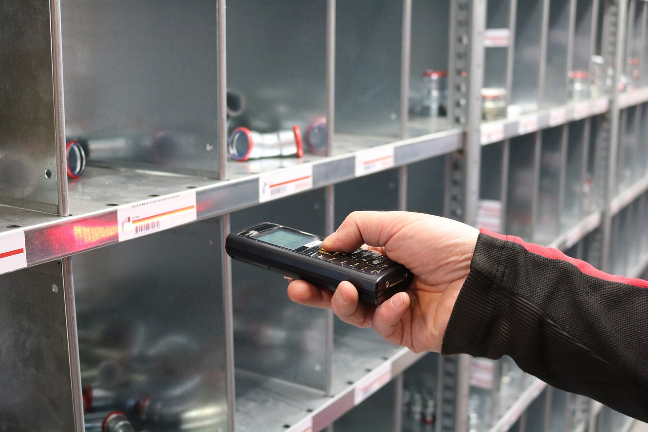 A business owner examines inventory on a shelf while holding a cell phone, showcasing effective management practices.