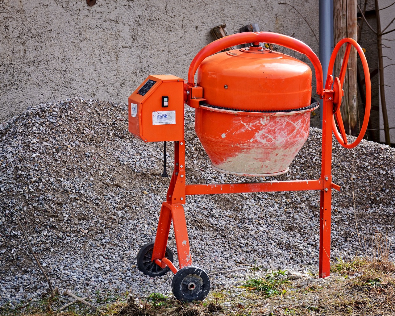 An orange cement mixer rests on a gravel mound , illustrating the work of a cement and concrete services business owner.